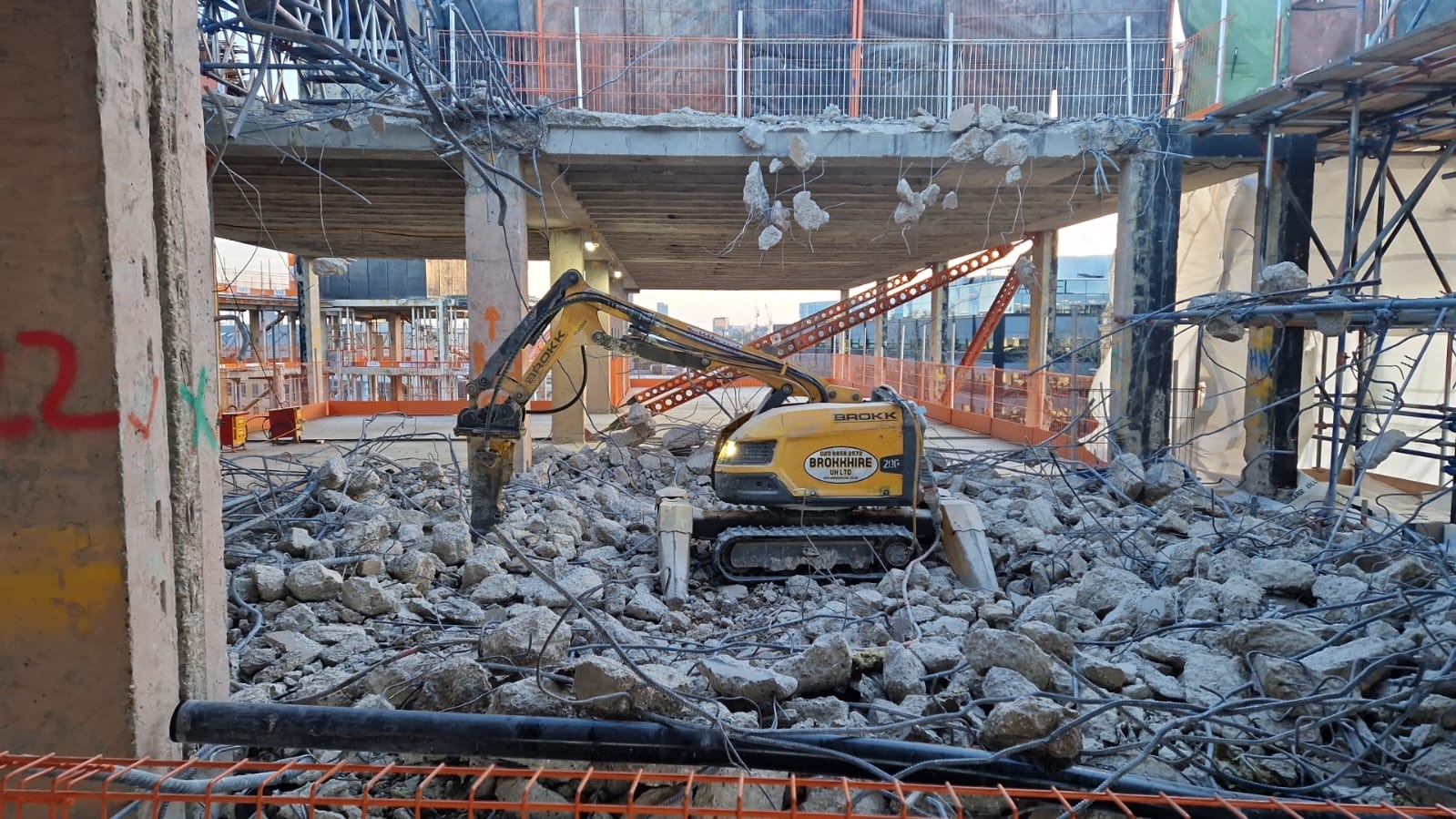Controlled Demolition Yellow demolition robot breaking concrete inside a partially demolished building, surrounded by rubble.