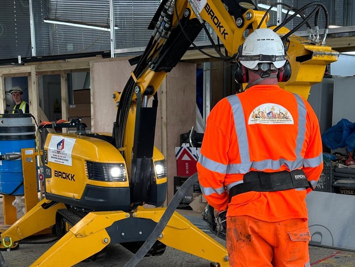 Demolition - Why Choose Us A construction worker in orange gear operates a yellow demolition machine indoors.