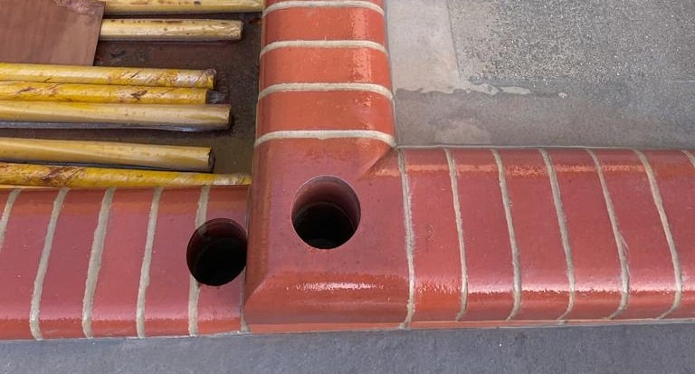 Diamond Core Drilling Red brick curb with two circular holes drilled at a corner; yellow rods lie nearby.