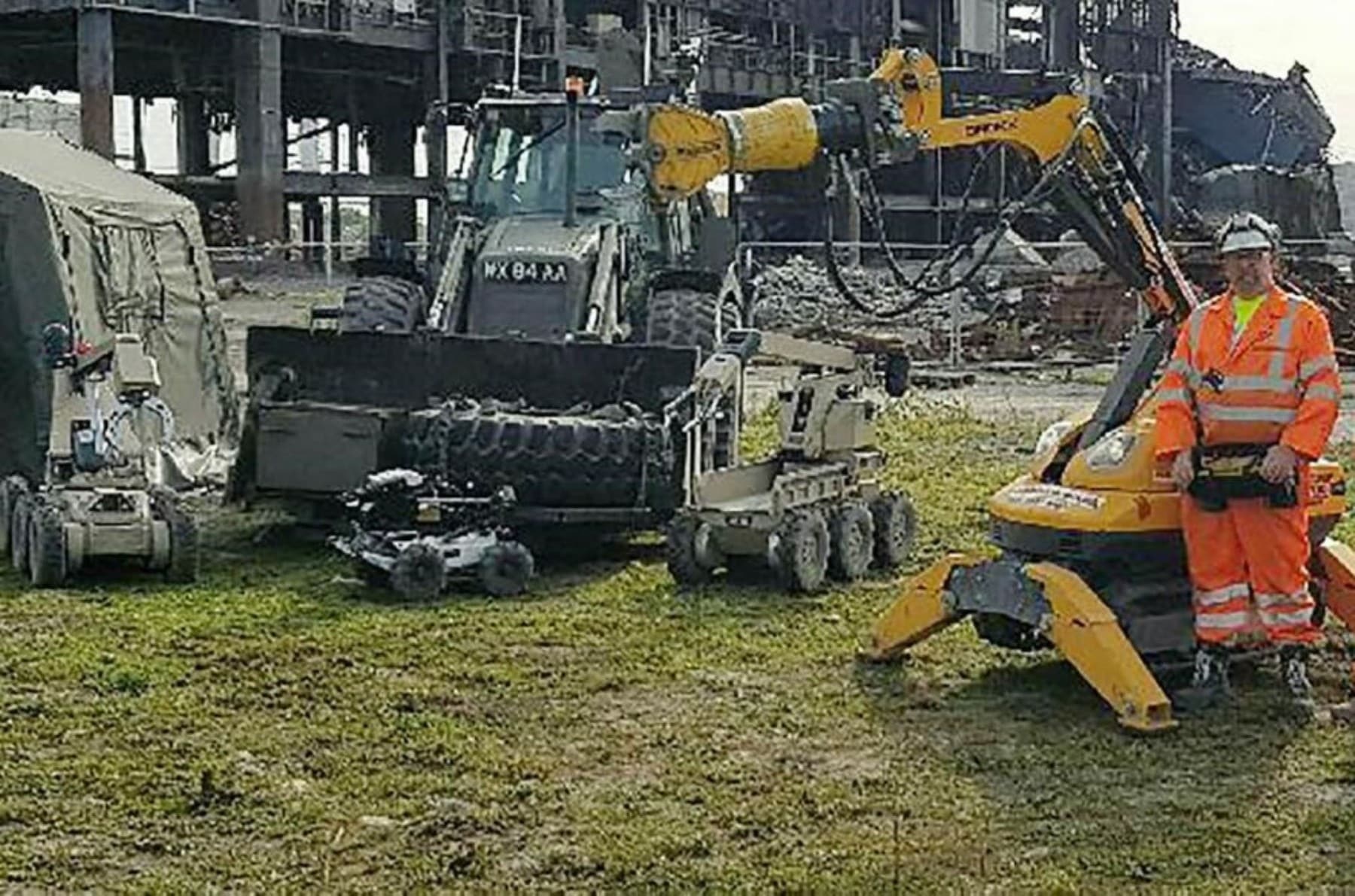 Didcot - Our Role Person in high-visibility gear stands with demolition robots and machinery at an industrial site.