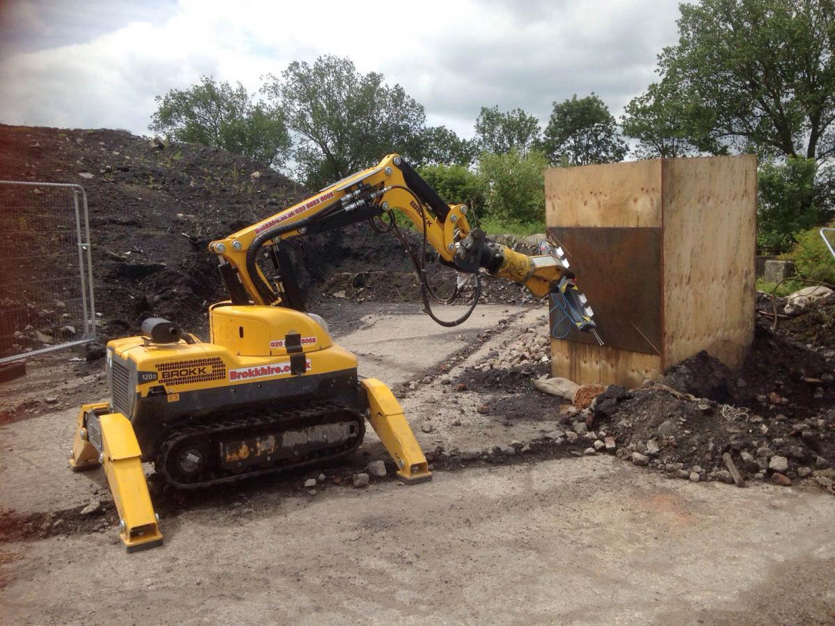 Didcot - Our Work Yellow construction robot working near a wooden box at an outdoor excavation site.
