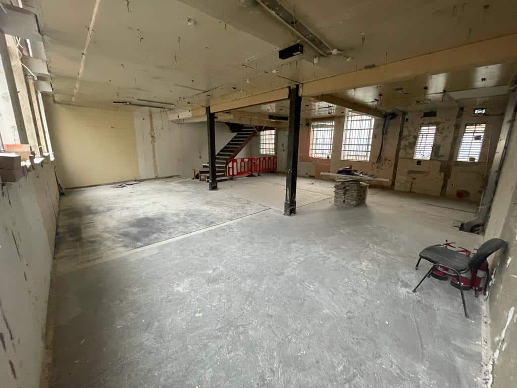 Empty, unfinished industrial space with bare walls, exposed beams, and construction materials.