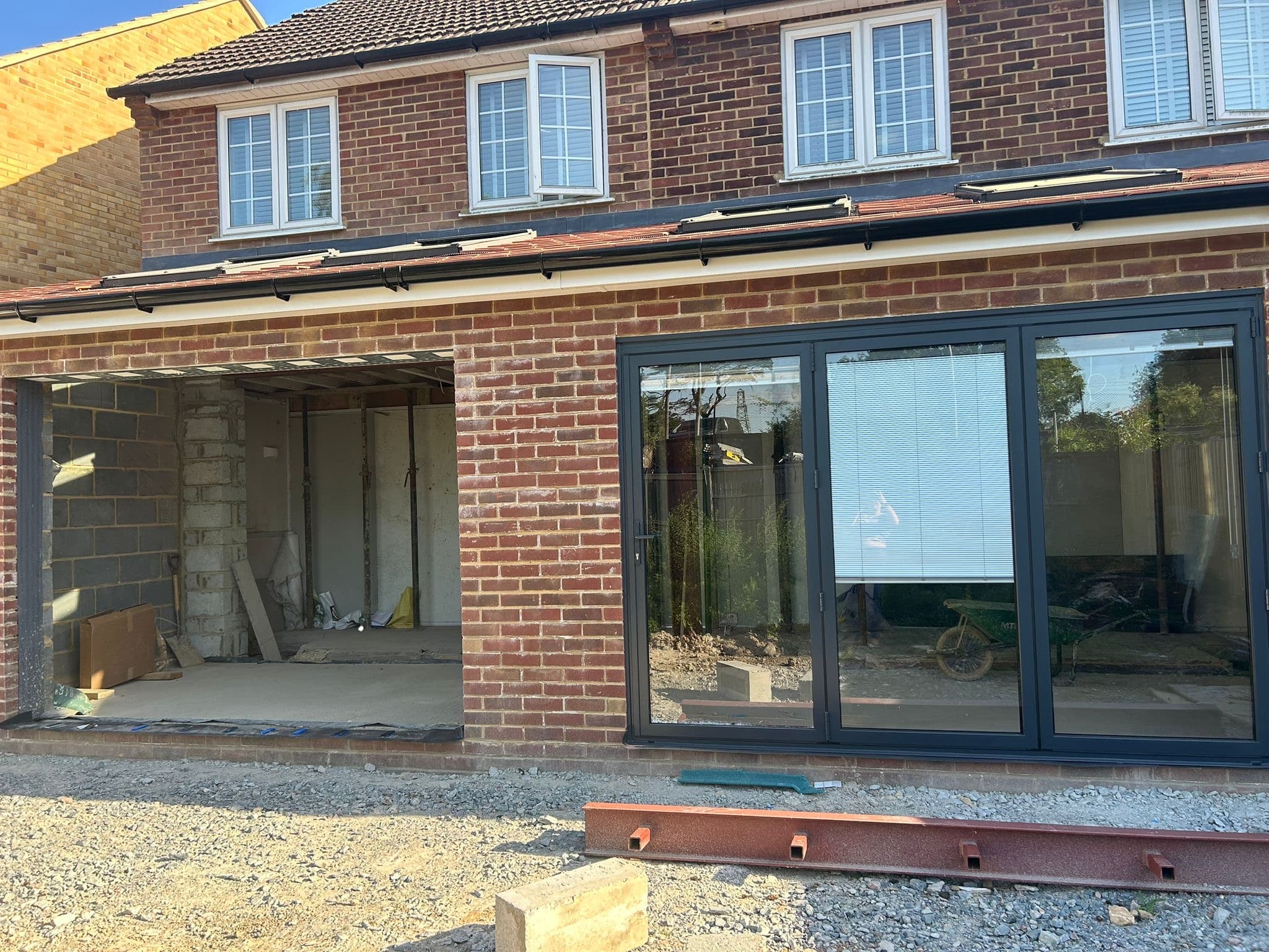 Brick house under renovation with large black-framed glass bifold doors and open unfinished area.