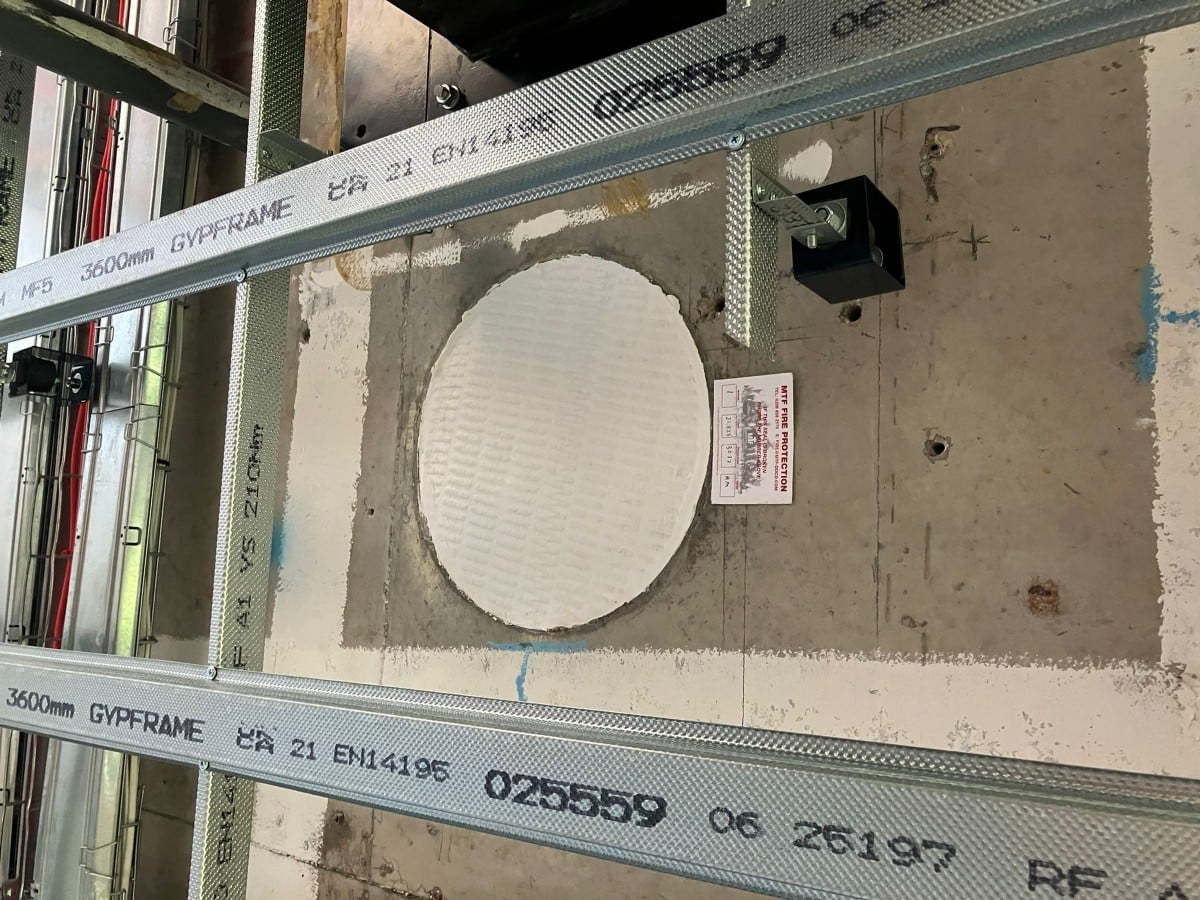 A circular fire sealant applied around a wall opening, with metal framing above and below.