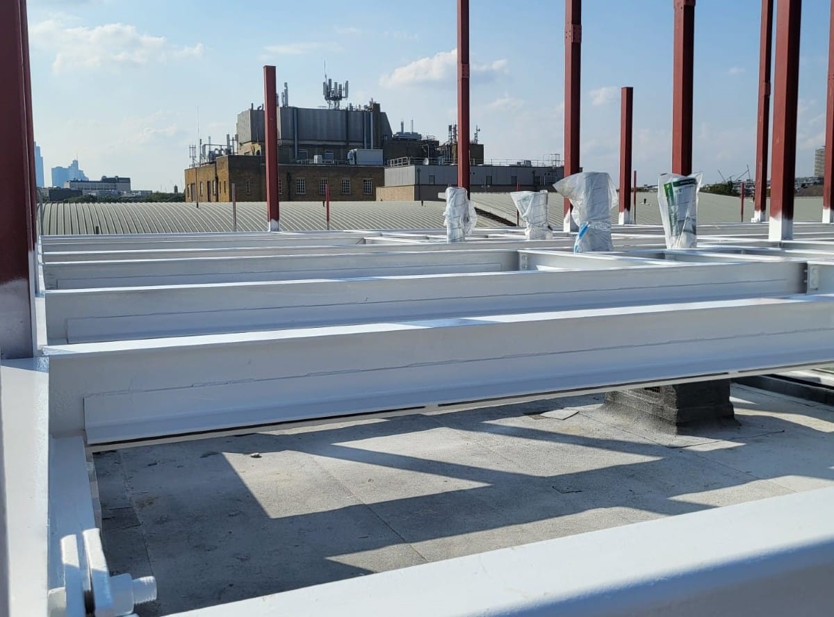 White flame-retardant coated steel beams on a rooftop construction site under a blue sky.