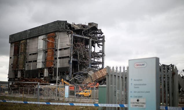 Didcot power station building collapse A partially collapsed industrial building behind a fence under a cloudy sky.