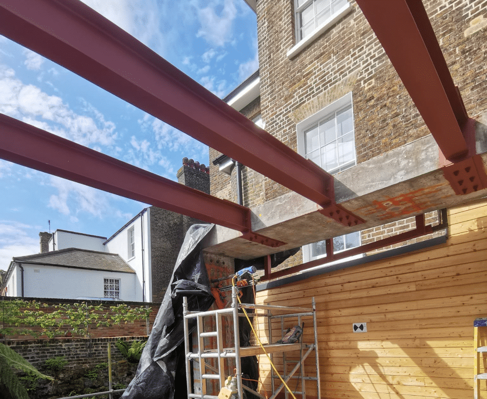 Steel beams installed at a building site, scaffolding below, brick and wood walls in background.