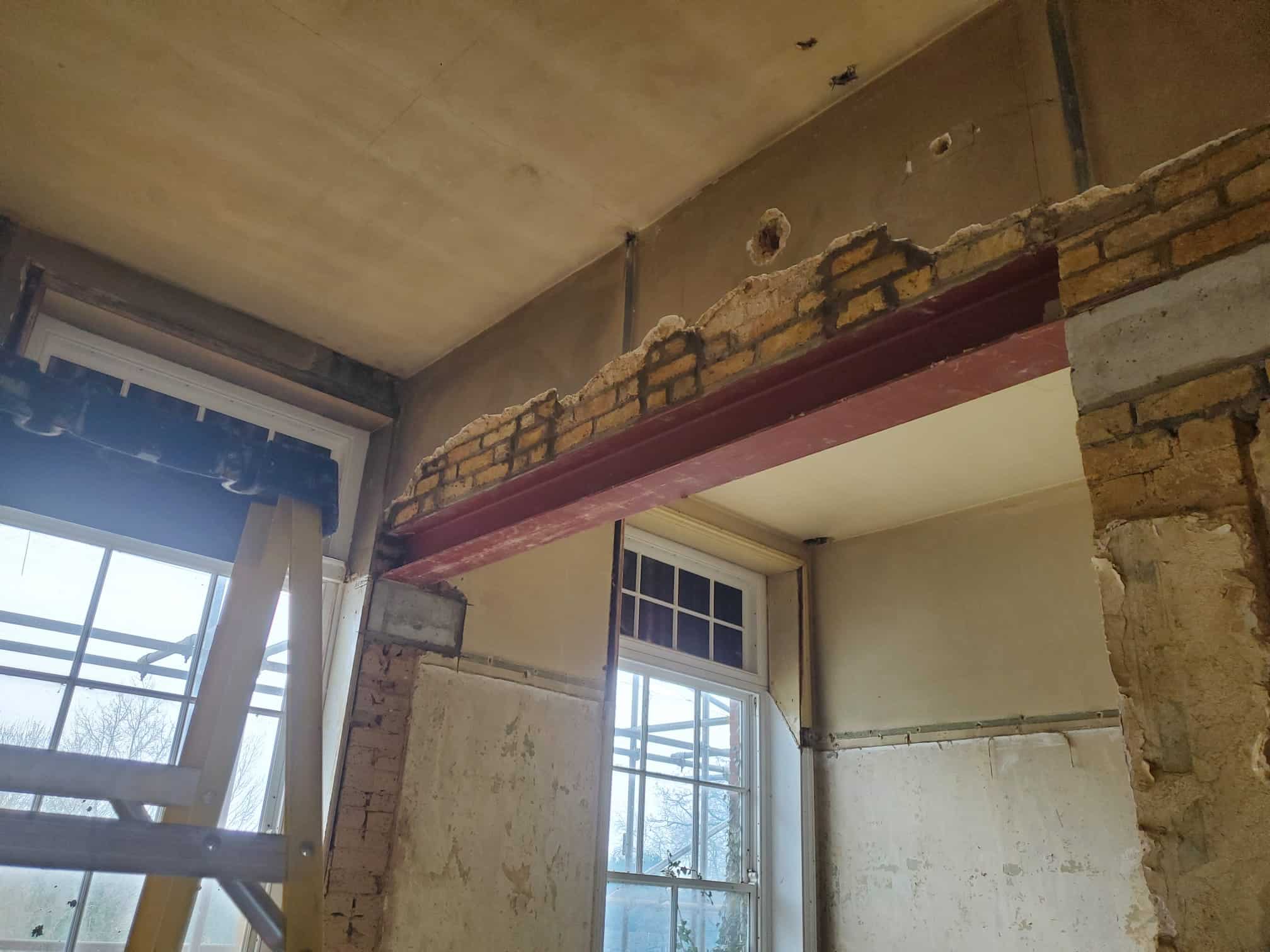 Steel beam installed in a partially demolished brick wall inside a building under renovation.