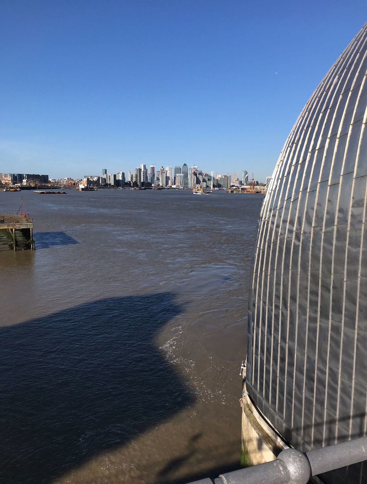 View of the Thames Barrier with city buildings in the distance under a clear blue sky.