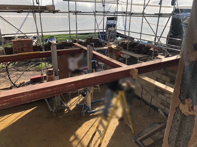 blursteels Steel beams being installed on a construction site with scaffolding and brickwork in progress.