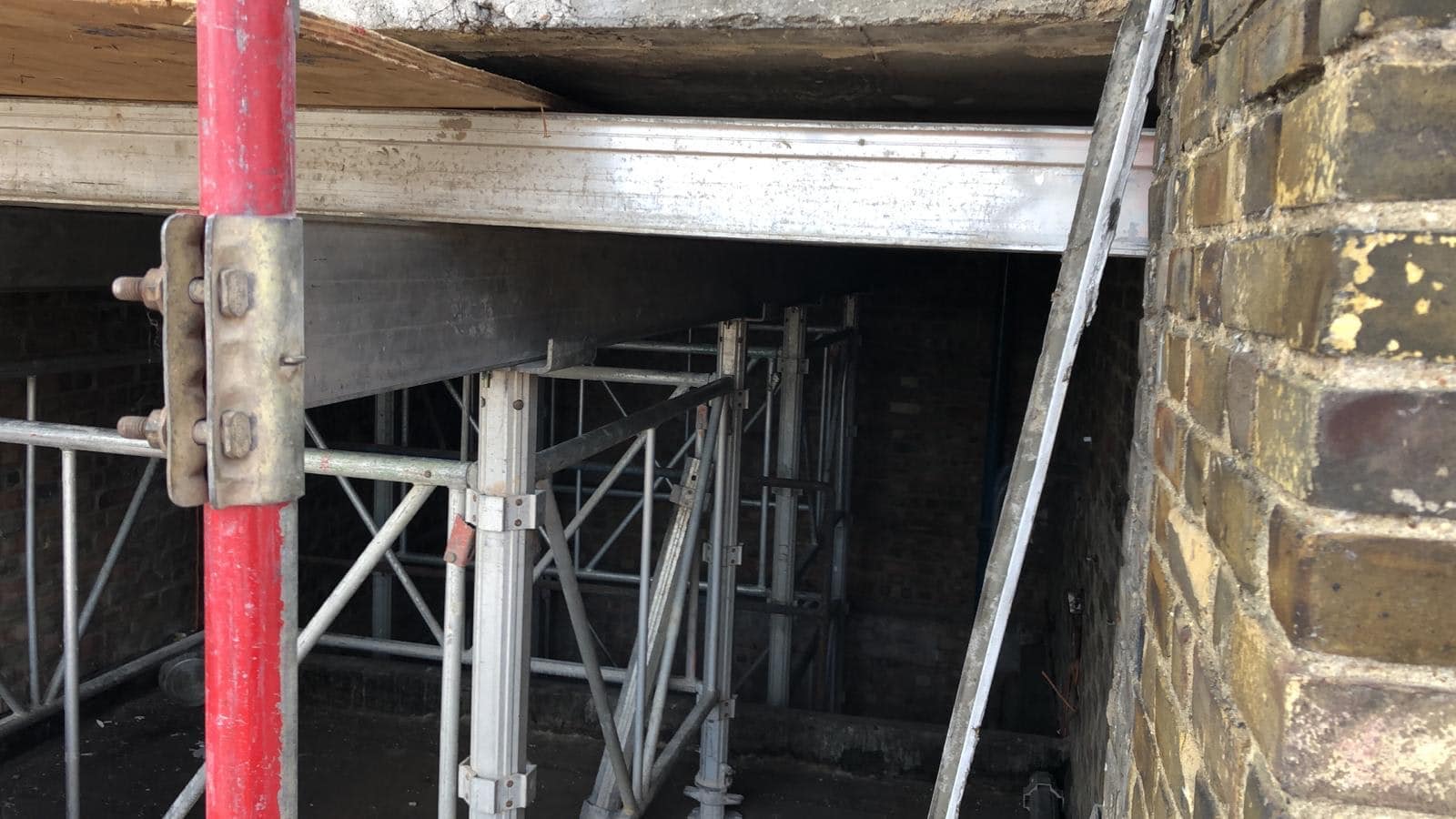 Scaffolding supports a building under construction beside a brick wall.