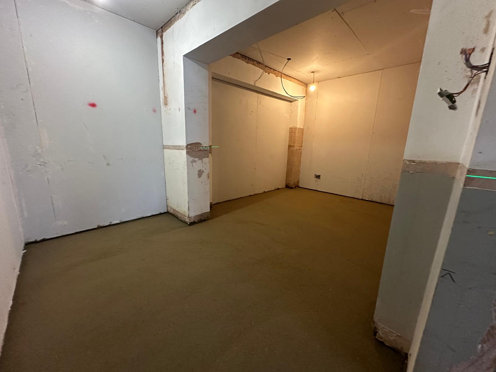 A room with freshly screeded floor and plain walls, lit by ceiling lights.
