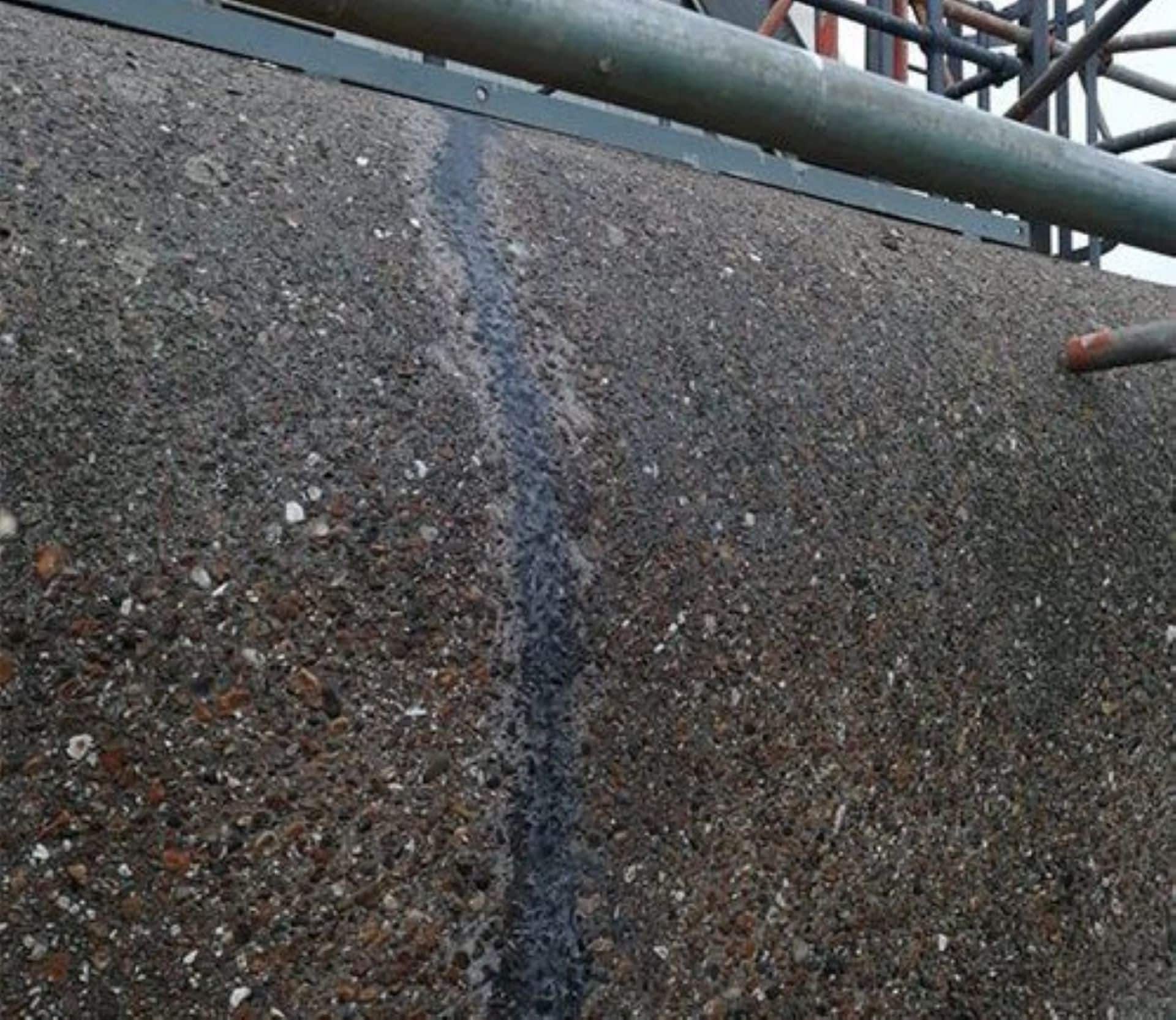 concrete repair Crack in a concrete wall repaired with a visible sealant line, with scaffolding above.