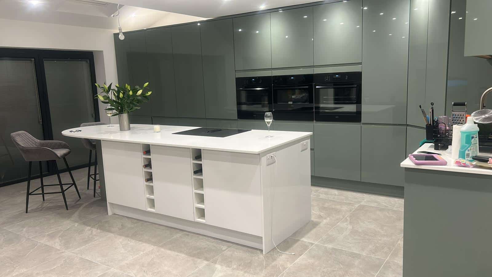 Modern kitchen with a white island, bar stools, and green cabinets.