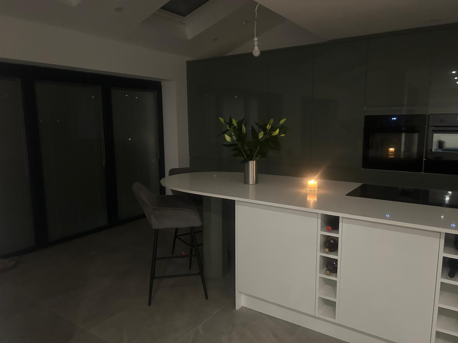 Modern kitchen with a white island, barstool, flowers in a vase, and a lit candle on the counter.