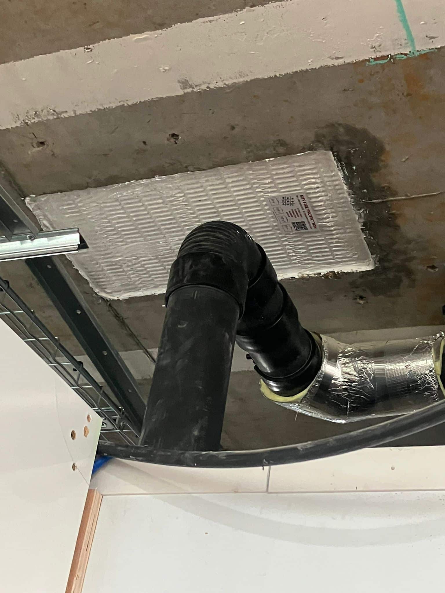 firestopping 06 Black pipes and a duct run below a firestopping board installed in a concrete ceiling.