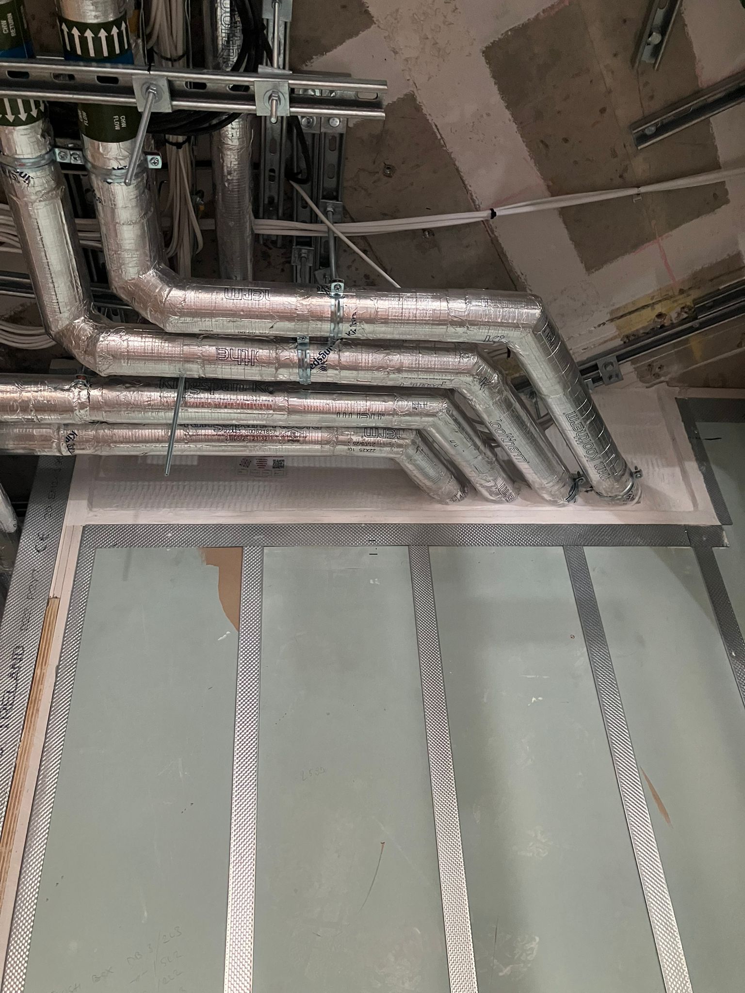 Silver pipes pass through a wall in a construction area with exposed metal framing and drywall.