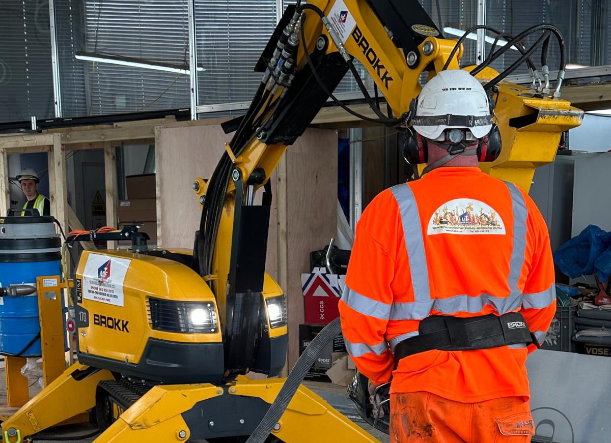 floor prep worker Worker in orange safety gear operating a yellow construction machine indoors.