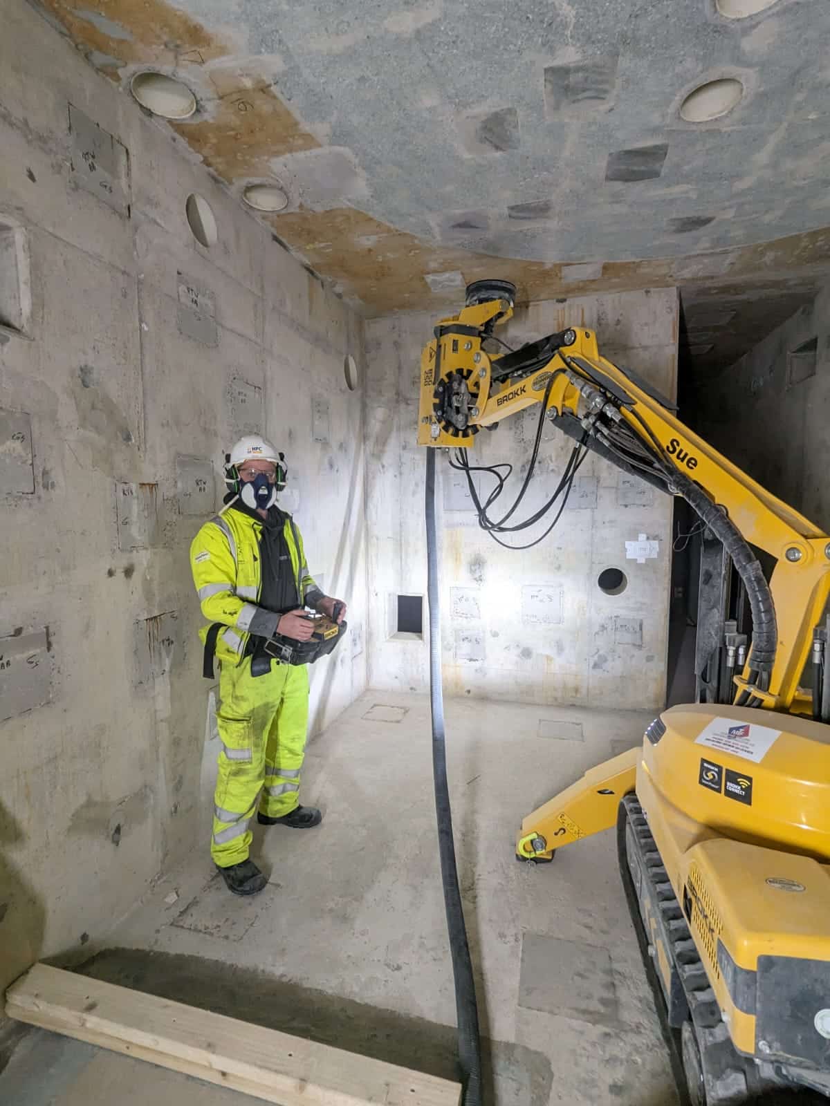floor prep Worker in safety gear operates a yellow construction machine inside a concrete room.
