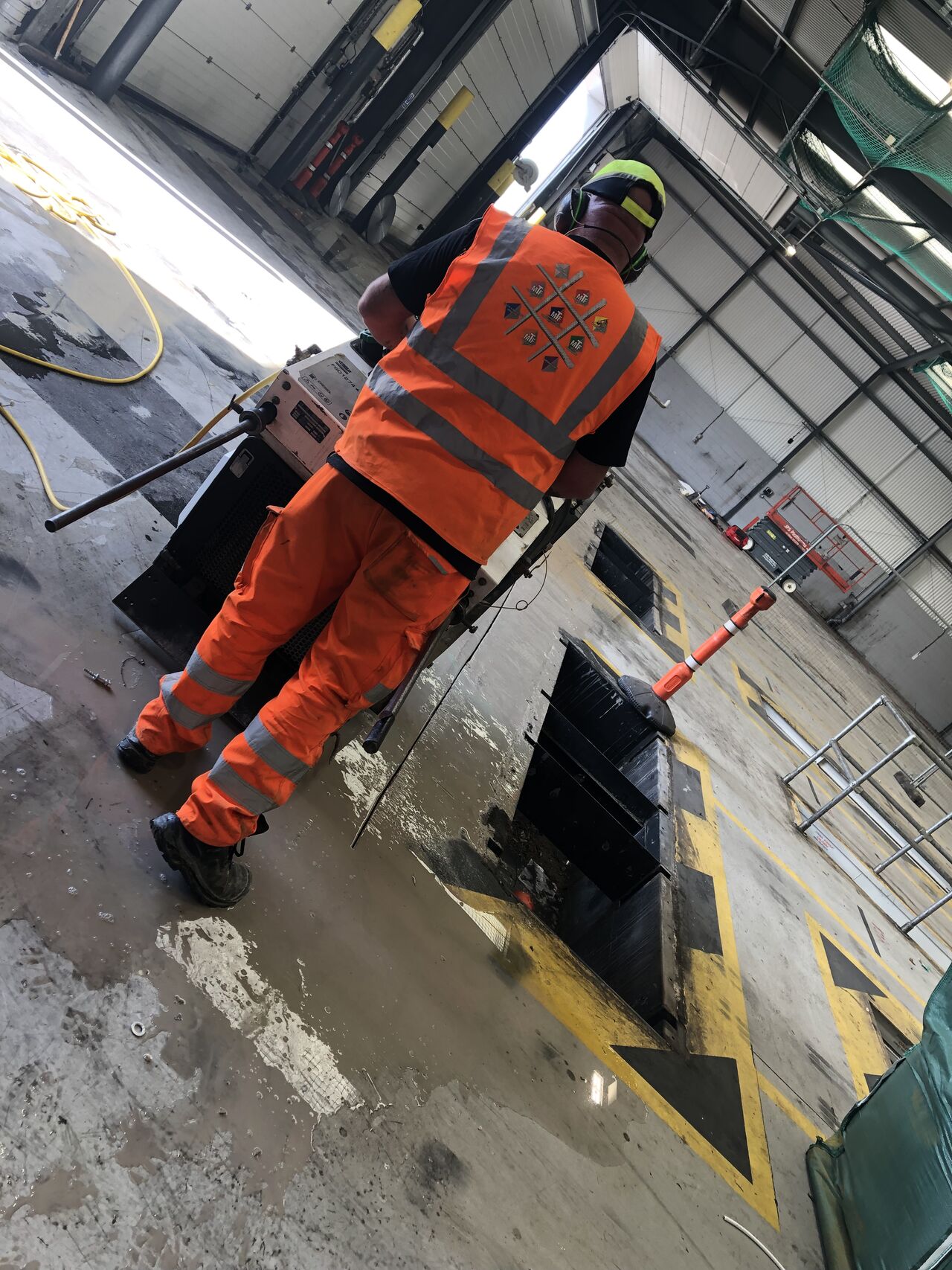 floorsaw3 Worker in orange safety gear operating a floor saw in an industrial warehouse.