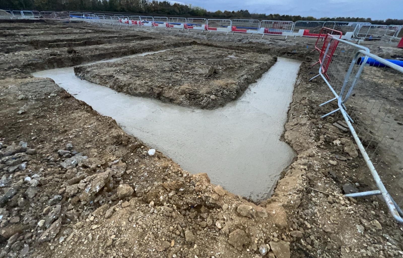 footings3 Concrete footing poured in a trench at a construction site with soil and safety barriers nearby.