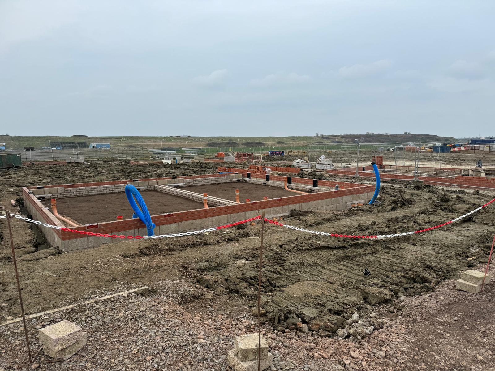 foundations4 Building foundations under construction on a muddy site with pipes and red bricks visible.