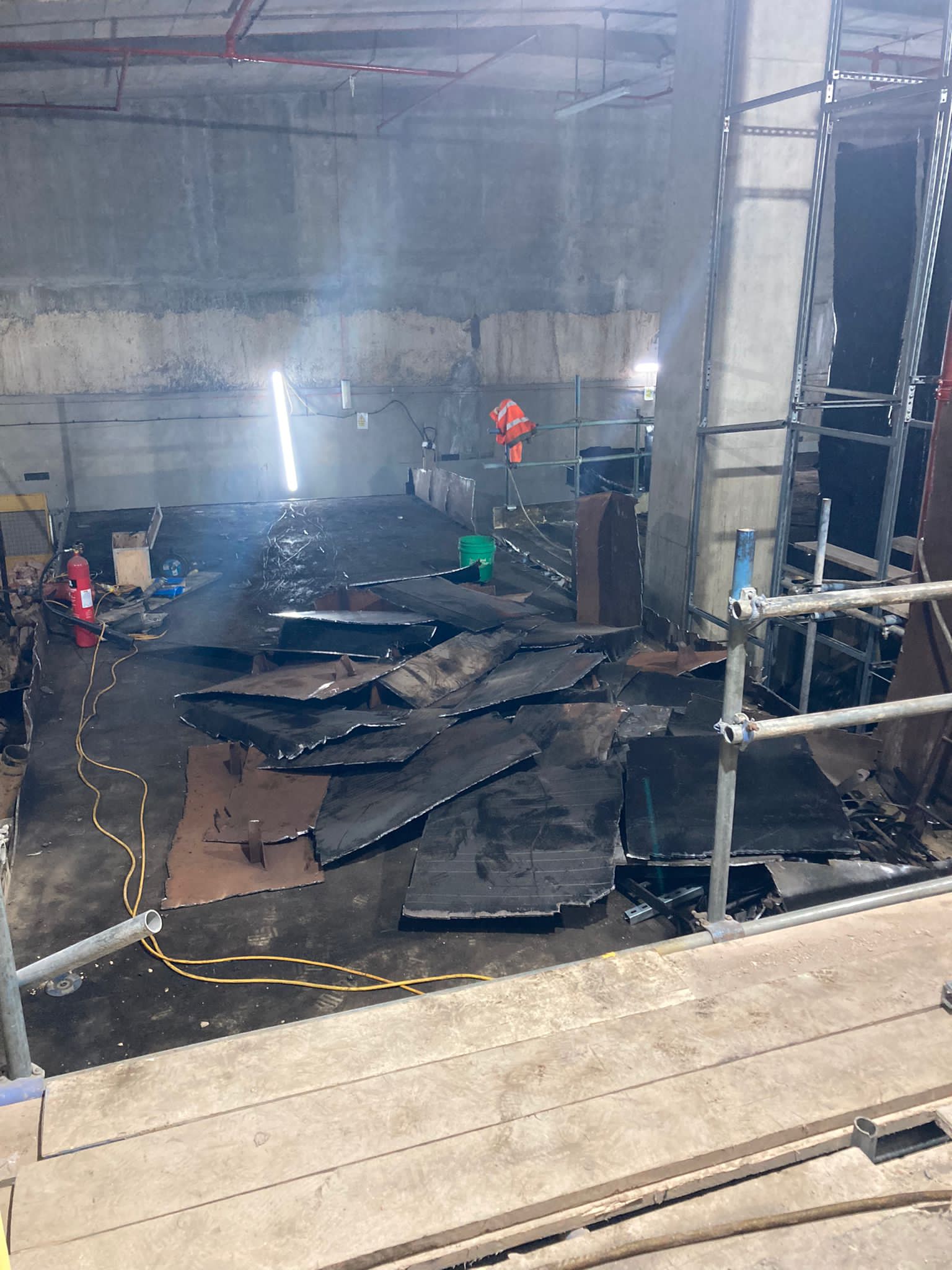 hammersmith Construction site with scattered metal sheets, scaffold, and bright work lights in a concrete room.