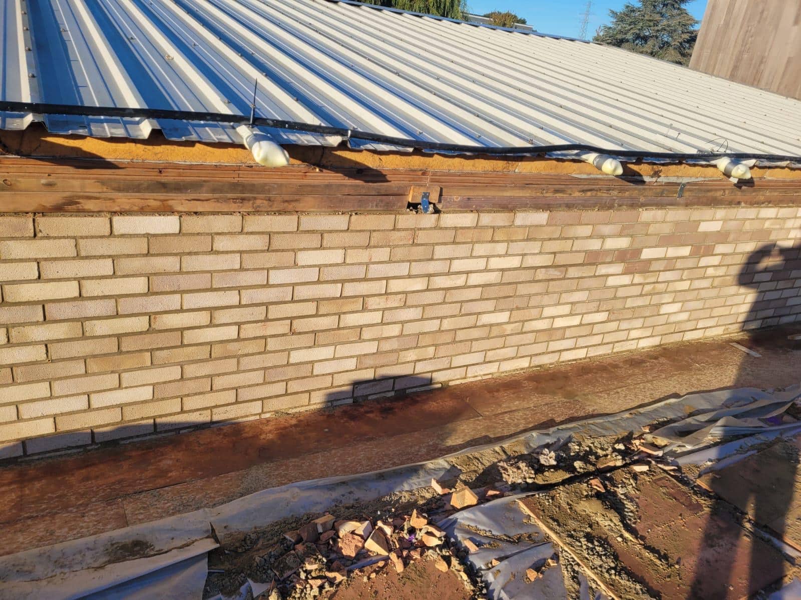 hounsdown Brick wall under a corrugated metal roof, with construction materials on the ground.