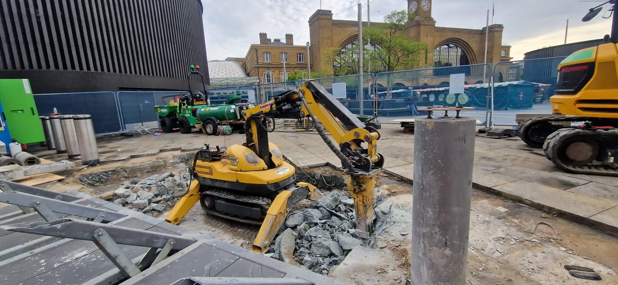 kingscrosscivils Yellow excavator breaking concrete at a construction site near King's Cross station.