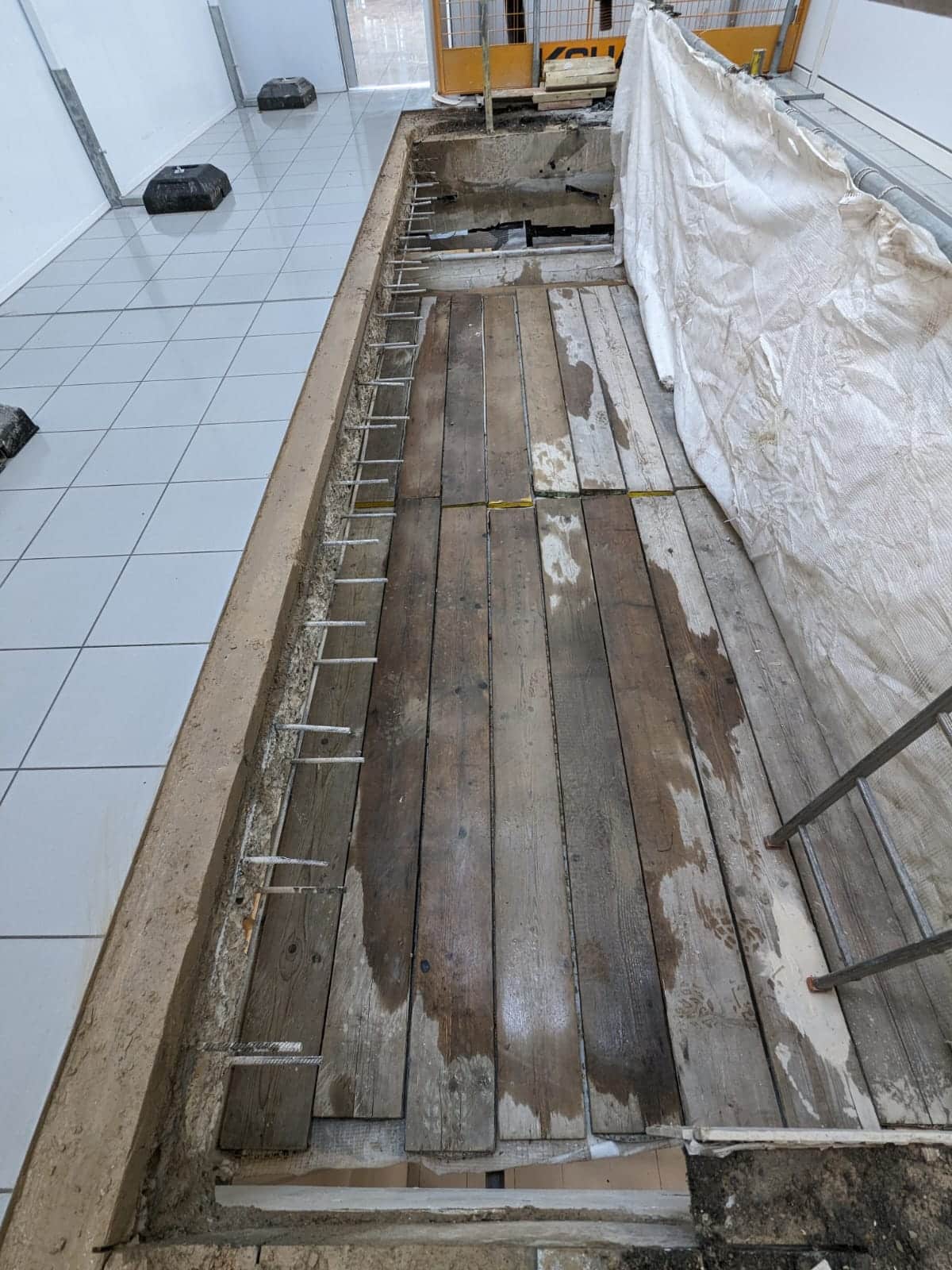 Old wooden floorboards exposed in an indoor space with tiled flooring nearby.