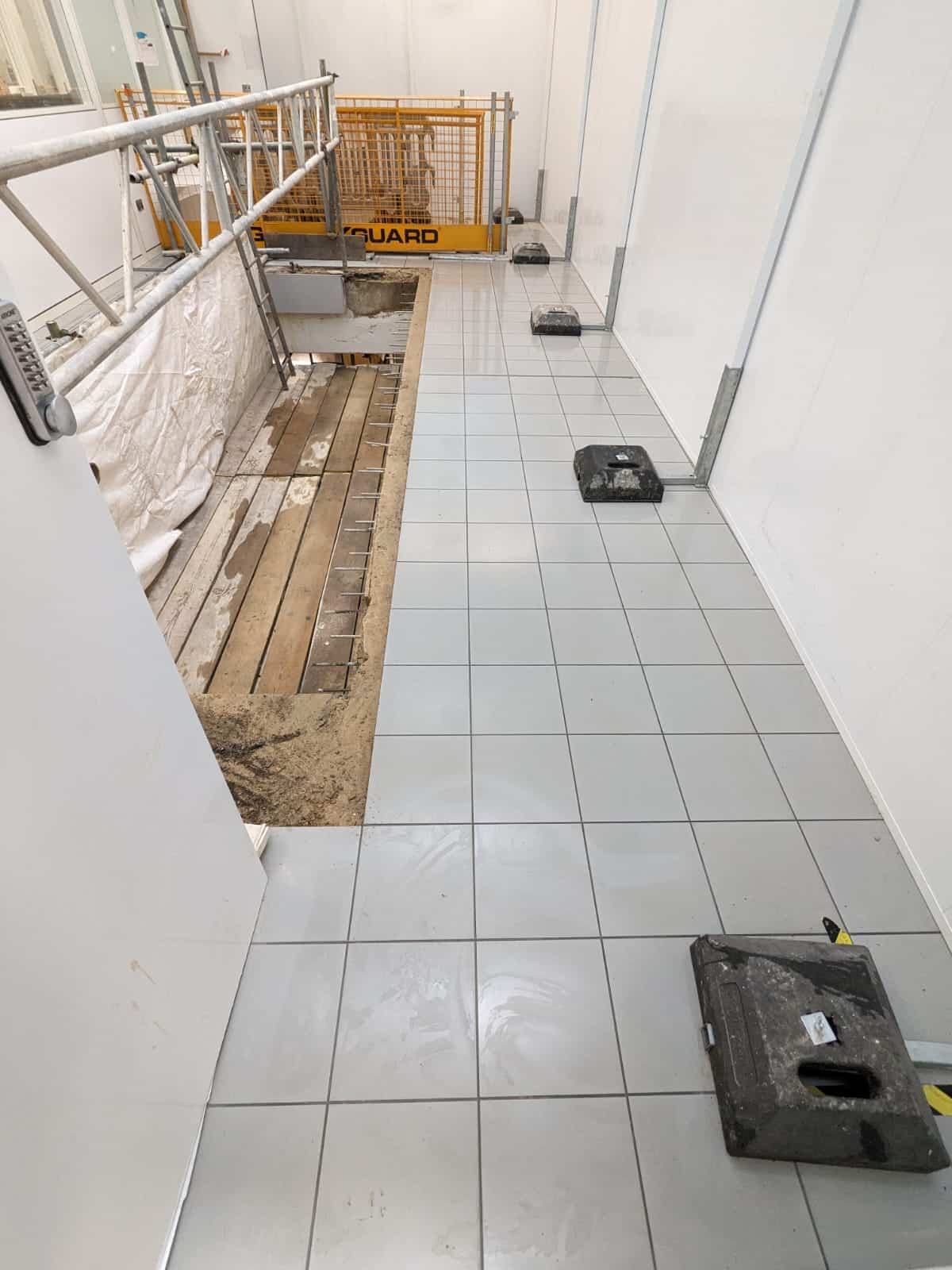 A tiled floor under construction with some tiles missing and construction materials nearby.