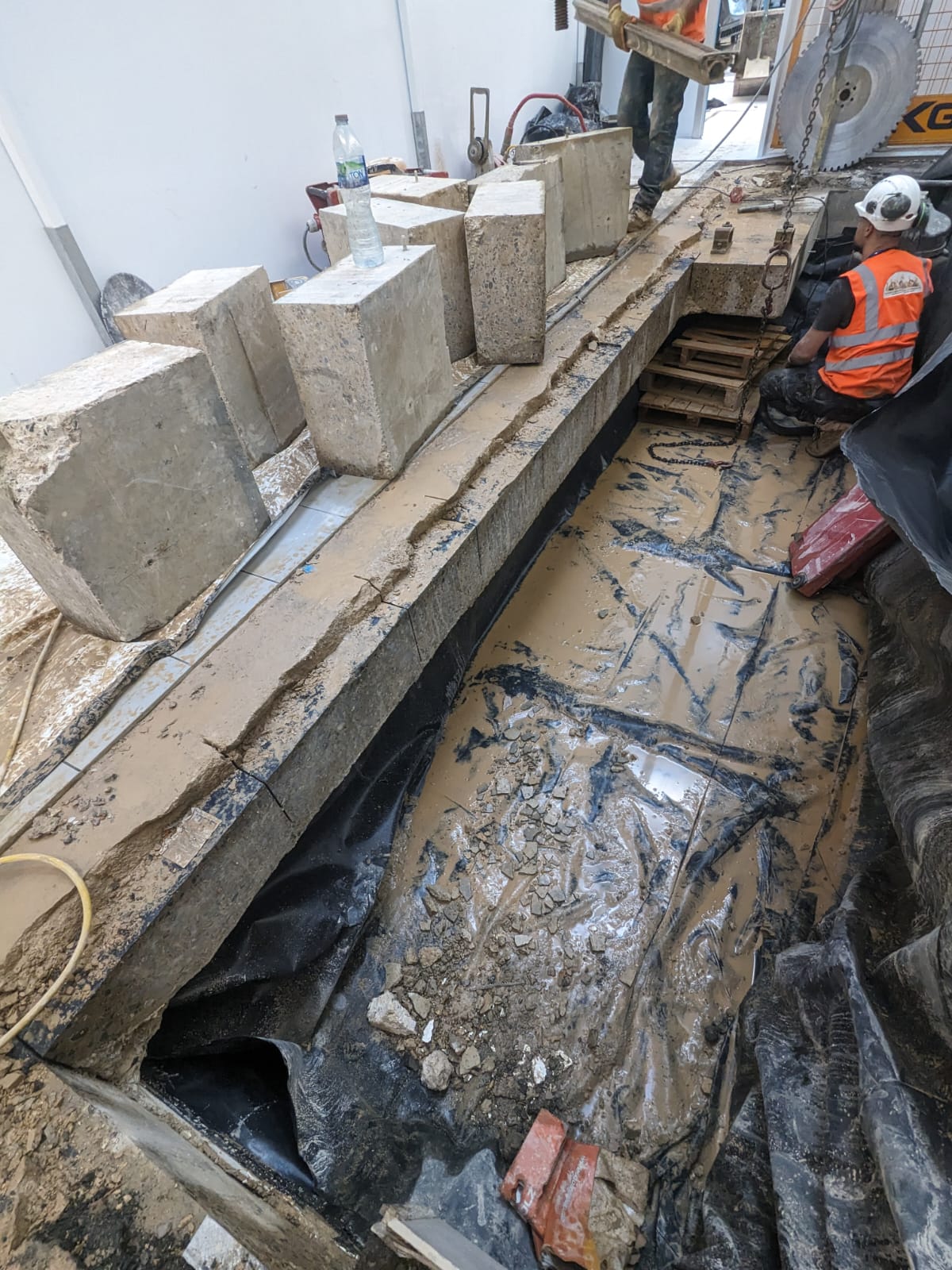 Construction site with concrete blocks, muddy ground, and a worker in an orange vest.