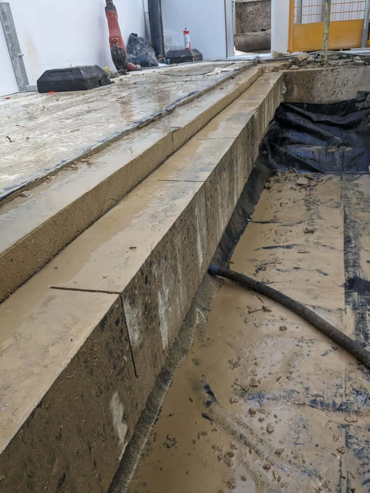 Construction site with muddy concrete forms and a hose on the ground.