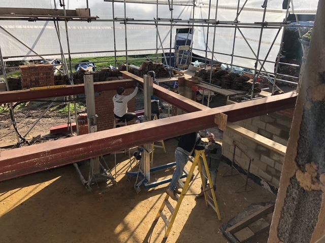 Two construction workers assembling steel beams inside a building under scaffolding.