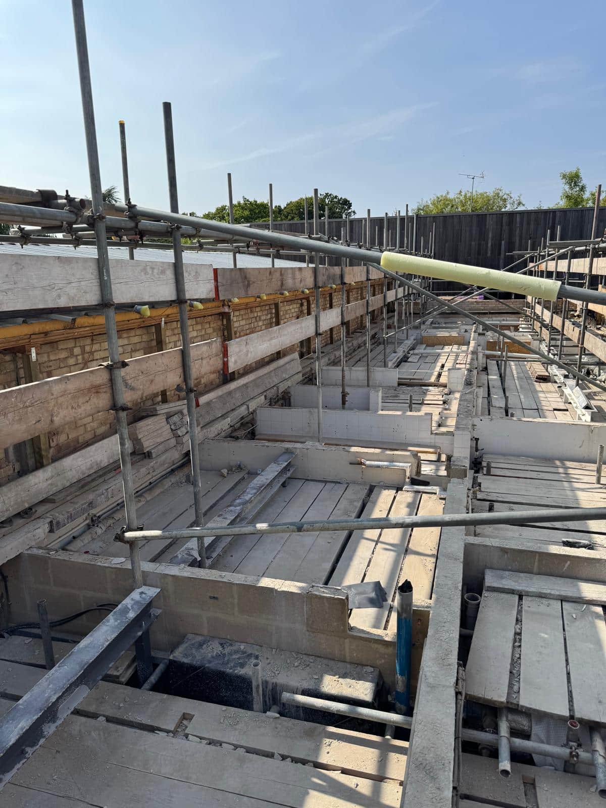 raac removal Construction site with exposed beams, scaffolding, and partial building framework under a clear sky.
