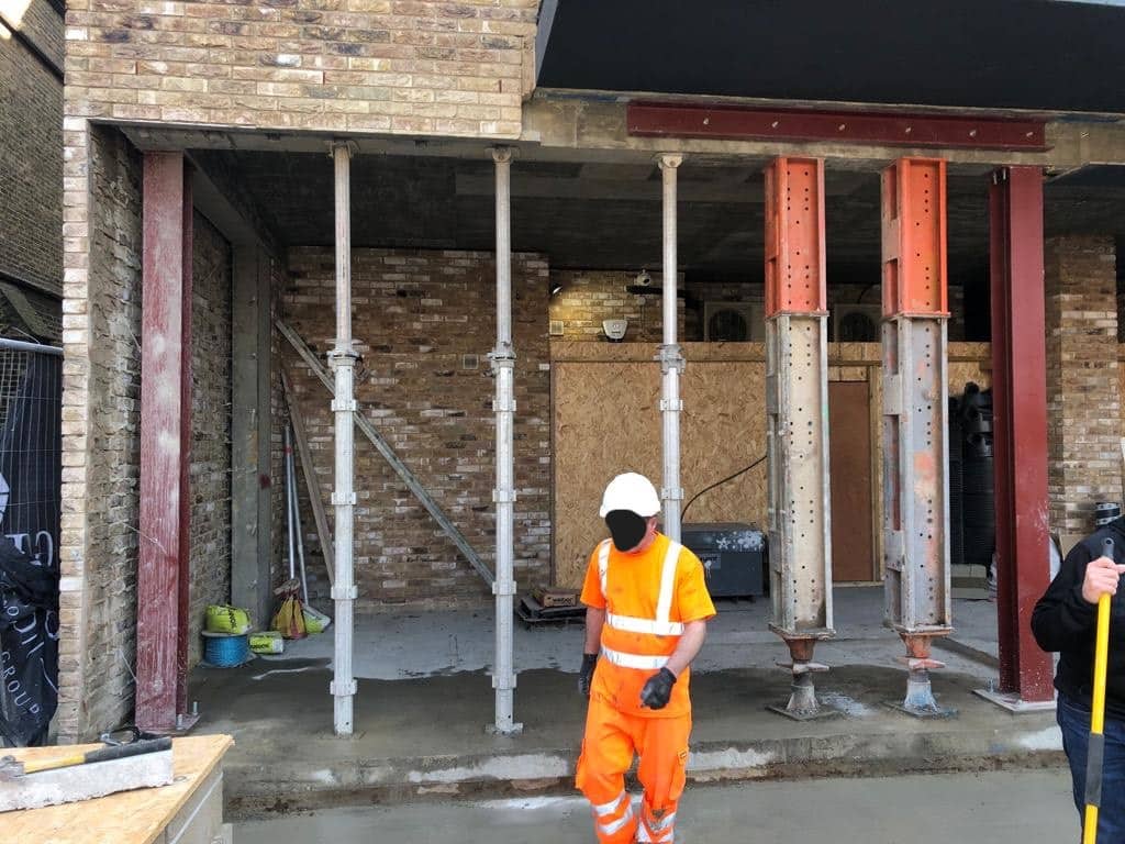 steels02edited Construction worker in orange safety gear stands in front of steel support beams at a building site.