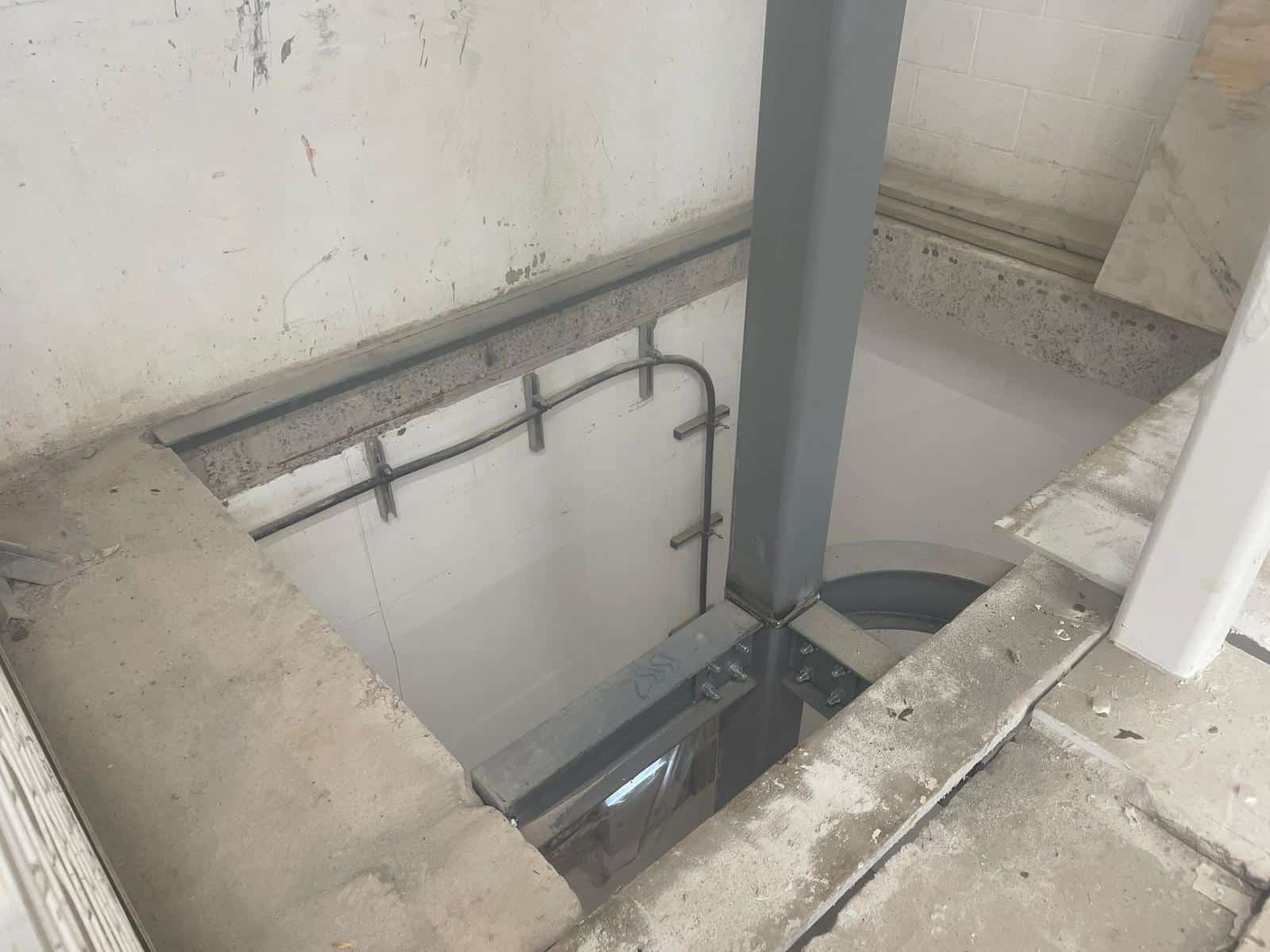 Steel beam structure installed in a concrete floor opening inside a building under construction.