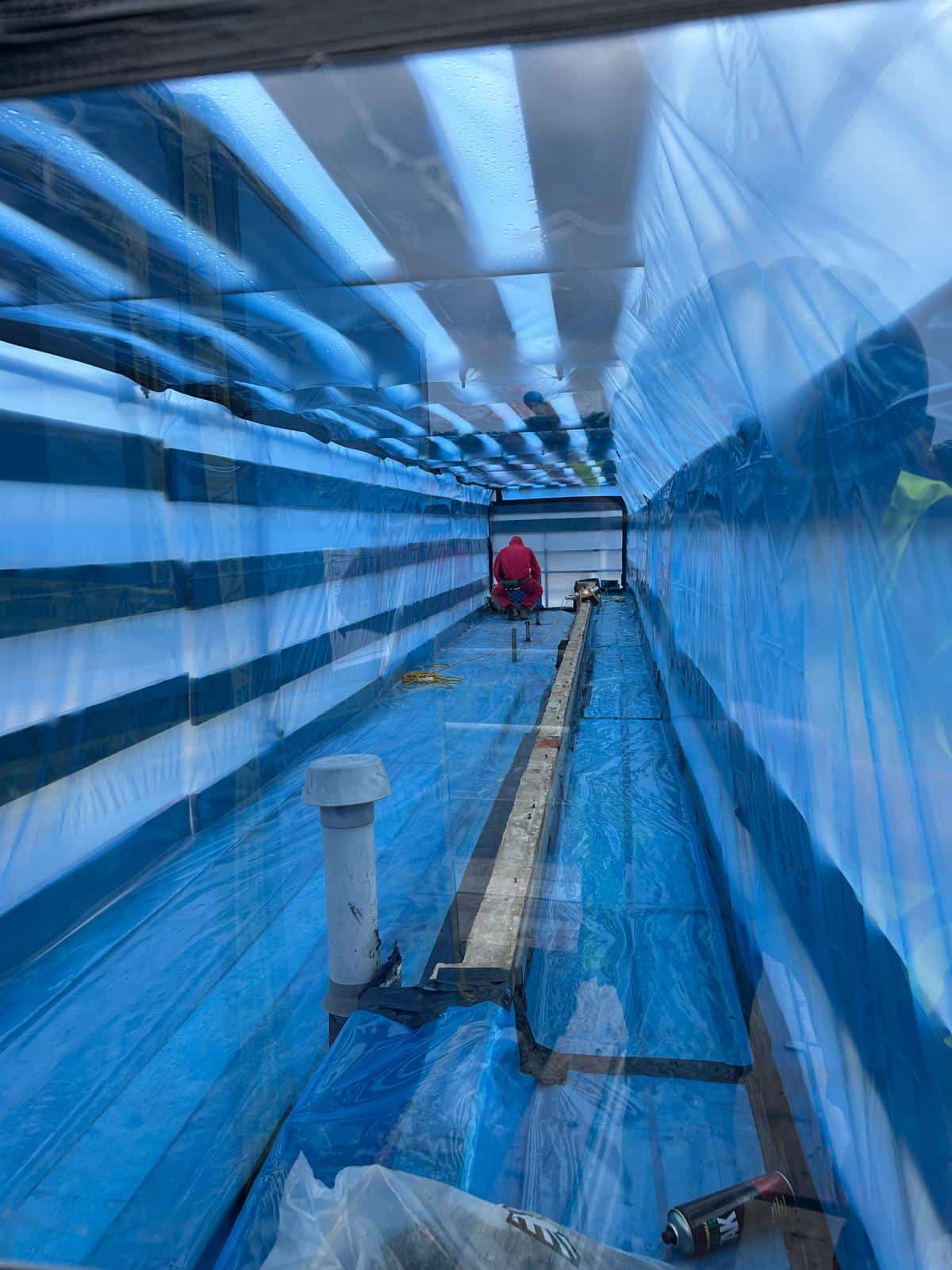 working with asbestos Worker in protective gear inside a blue plastic enclosure, possibly for asbestos removal.